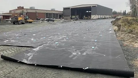 Stor flate dekket med sort duk på gruslagt underlag ved industriområde